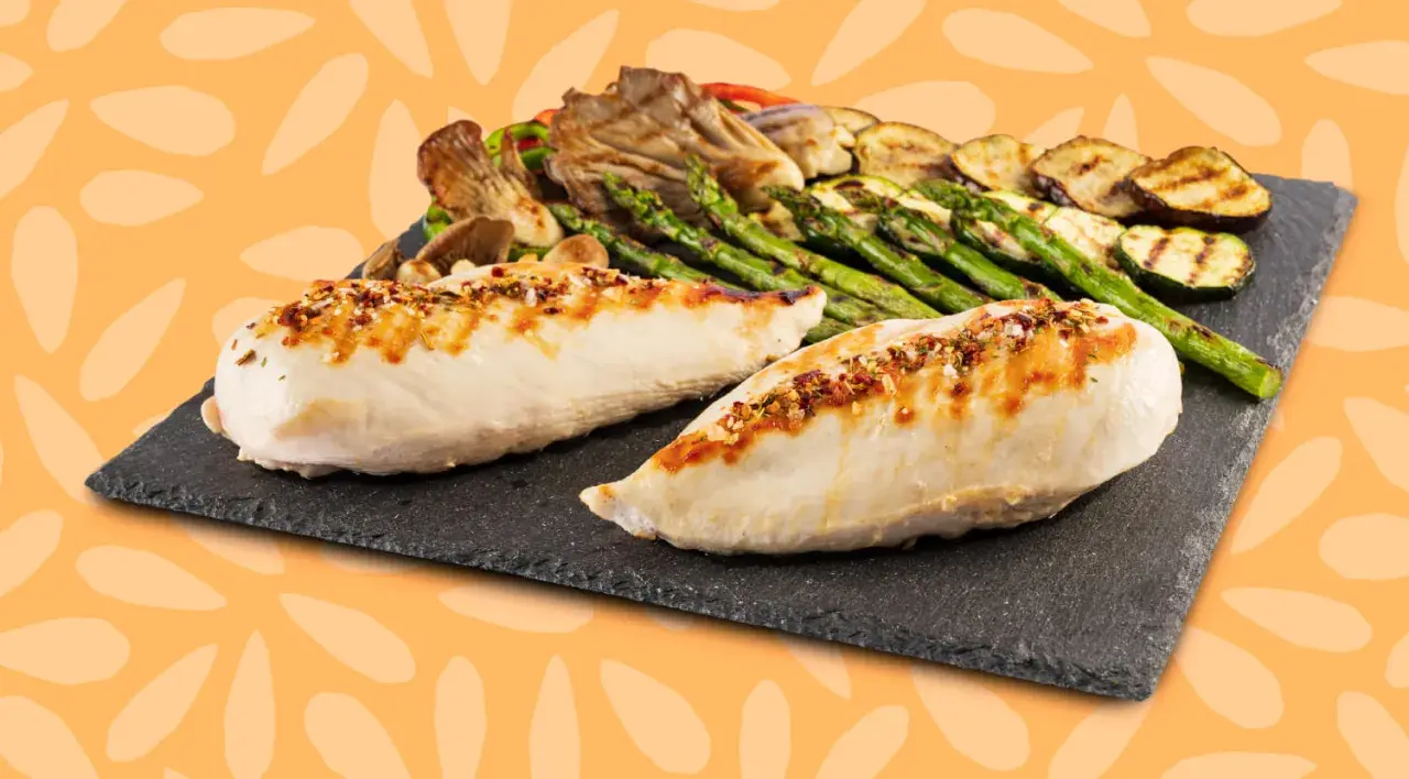 Dos jugosas pechugas de pollo a la parrilla, sazonadas con especias, acompañadas de espárragos, calabacín y champiñones.