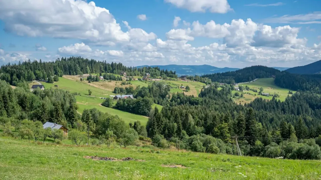 Zielone wzgórza Beskidu Wyspowego, pełne drzew i domków, pod błękitnym niebem z białymi chmurami.