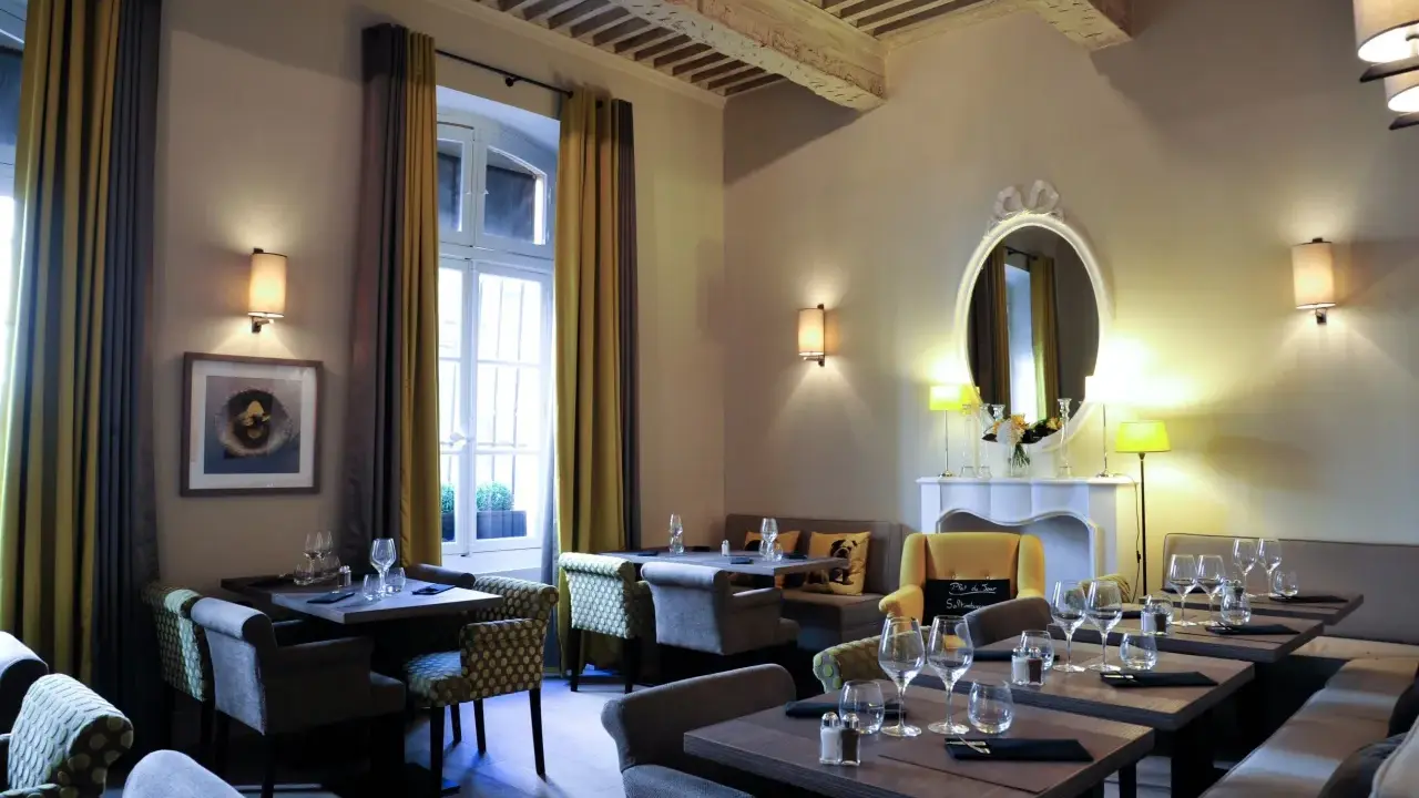 Salle à manger élégante avec tables dressées, fauteuils confortables et un miroir orné. L'ambiance évoque une **spécialité provençale** raffinée.