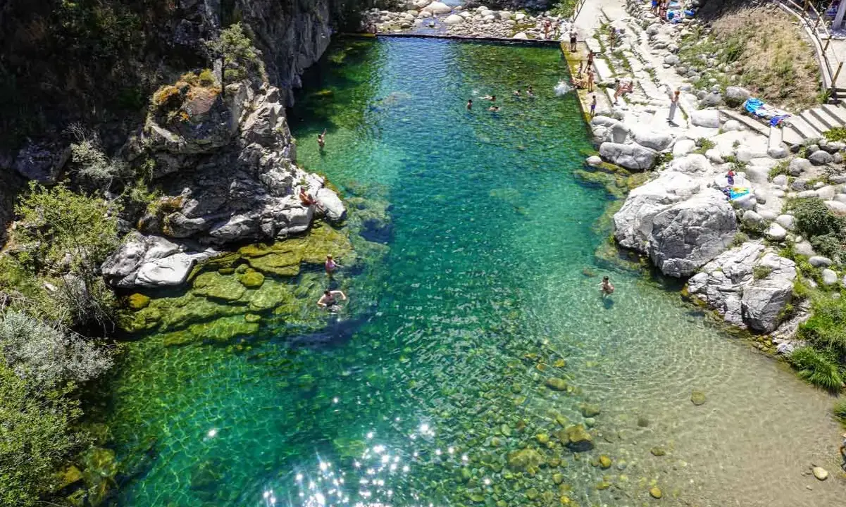Una espectacular piscina natural en Extremadura, con aguas cristalinas y gente disfrutando del baño entre rocas y vegetación.