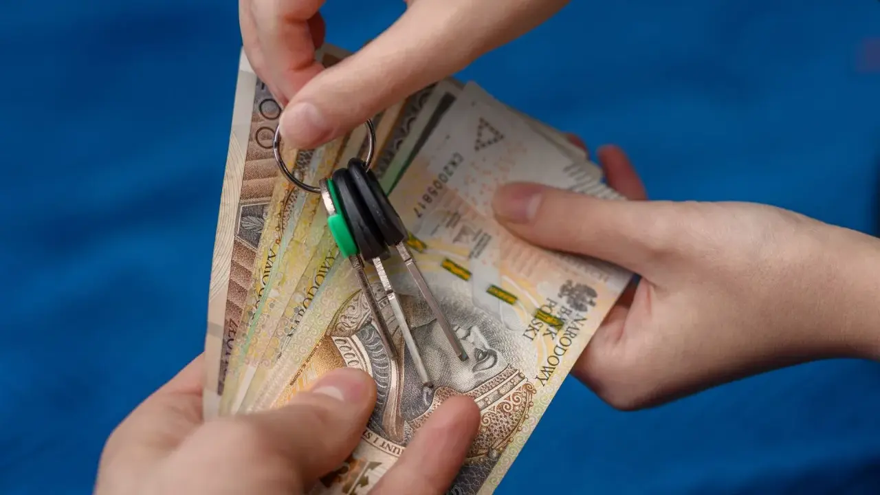 Dwie ręce trzymają plik banknotów i klucze. Zastanawiasz się, od jakiej kwoty płaci się podatek od wynajmu mieszkania?