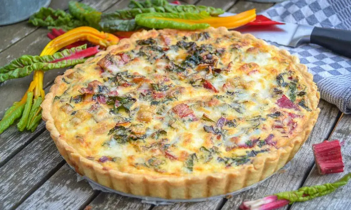 Herzhafte Quiche mit buntem Mangold und knusprigem quiche teig auf Holztisch, garniert mit frischem Mangold.