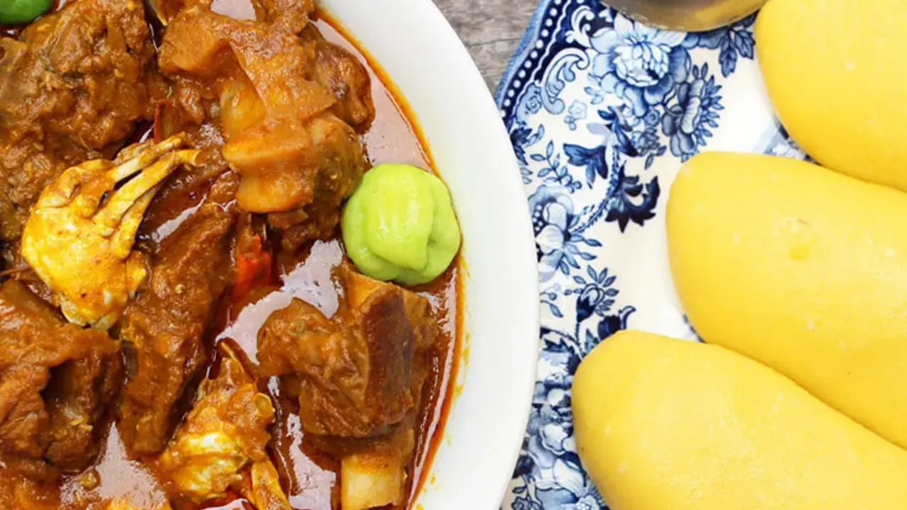 Un plat de foutou sauce graine avec de la viande et du crabe, accompagné de boules de pâte jaune sur une assiette décorée.