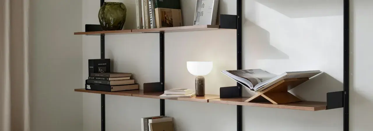 En stilren hylla i vardagsrummet med böcker, en vas och en lampa.