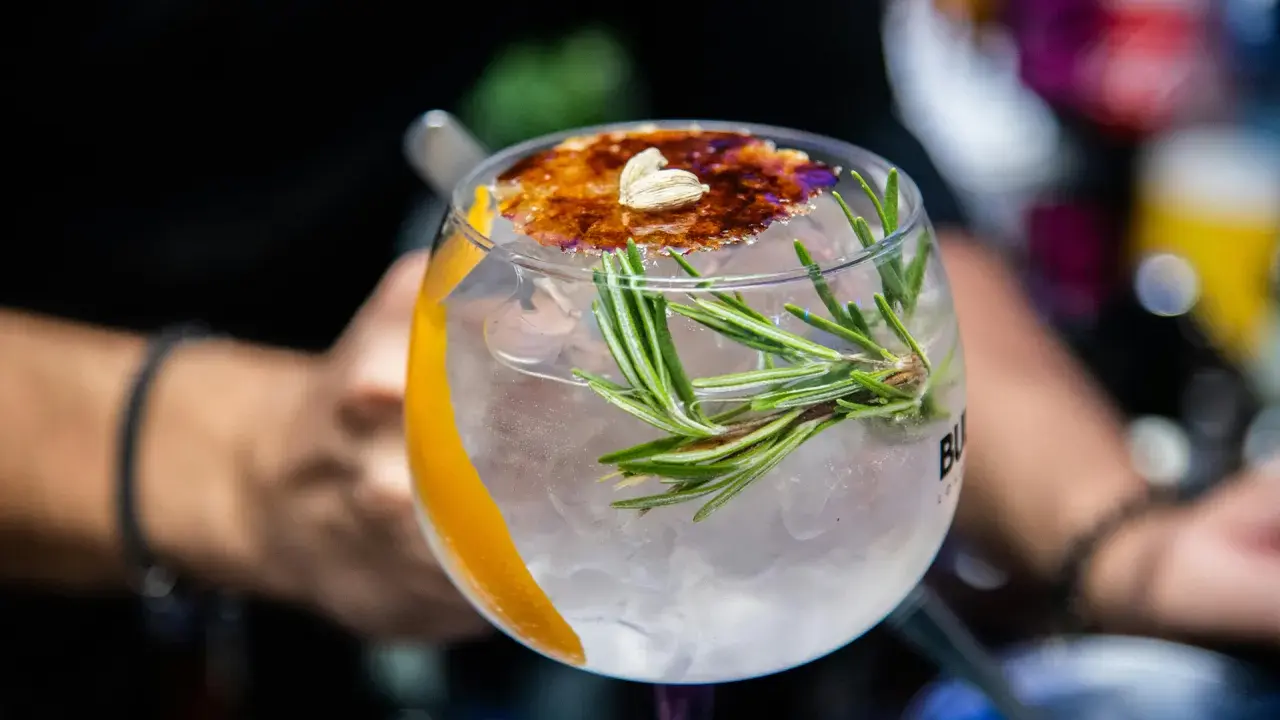 Ein erfrischender Gin Tonic, ein klassischer Cocktail, garniert mit Rosmarin, Orangenzeste und karamellisiertem Zucker.