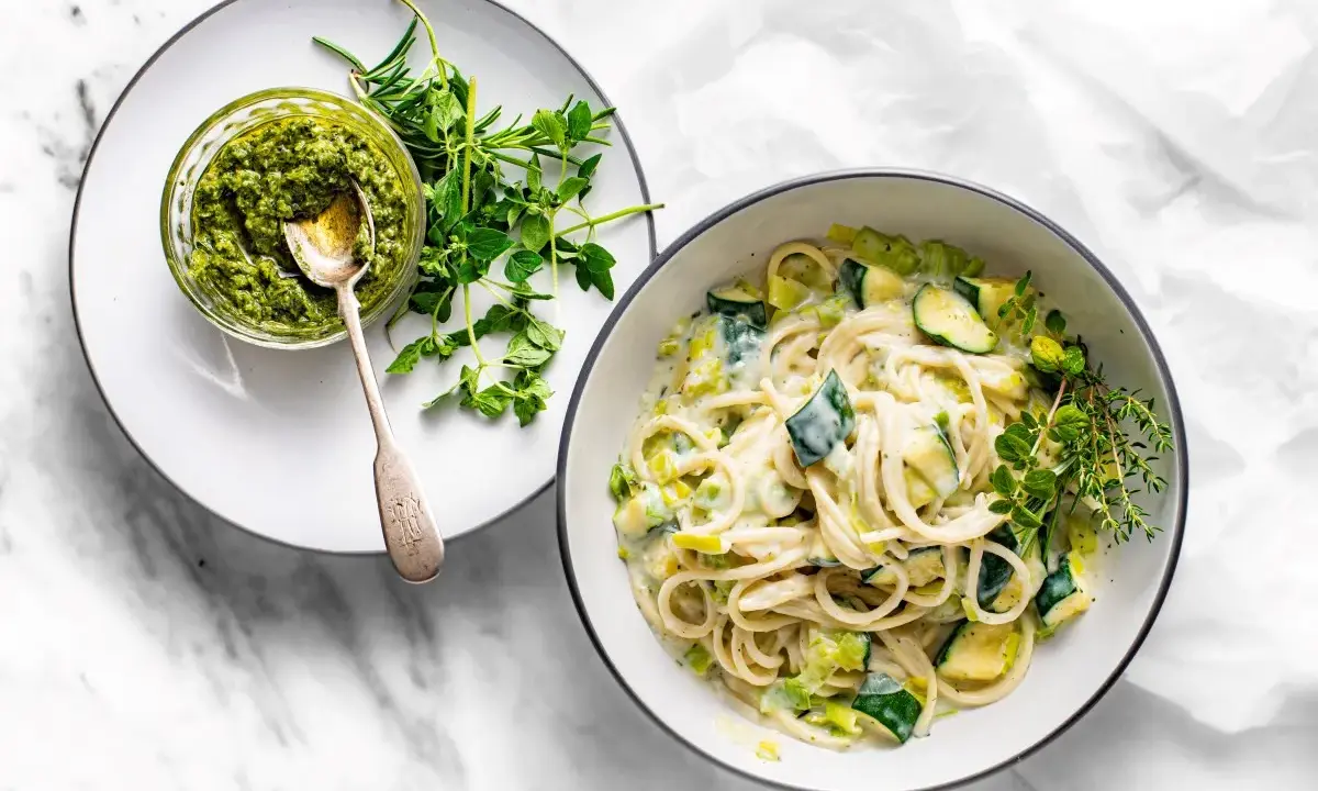Pyszny makaron z cukinią w kremowym sosie, obok miseczka pesto i świeże zioła. Idealny lekki posiłek.