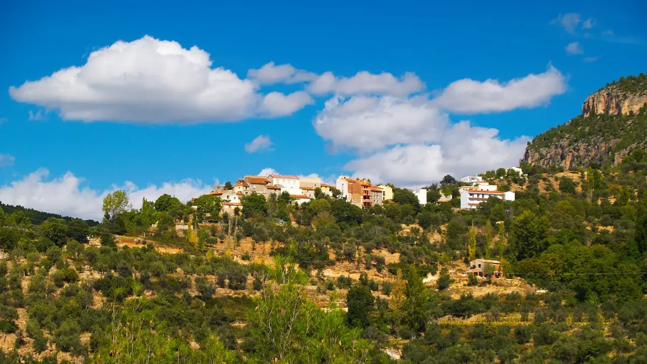 Pueblo blanco en la ladera de una montaña, rodeado de olivos y vegetación. El cielo azul con nubes blancas corona la vista de Gontar, Albacete.