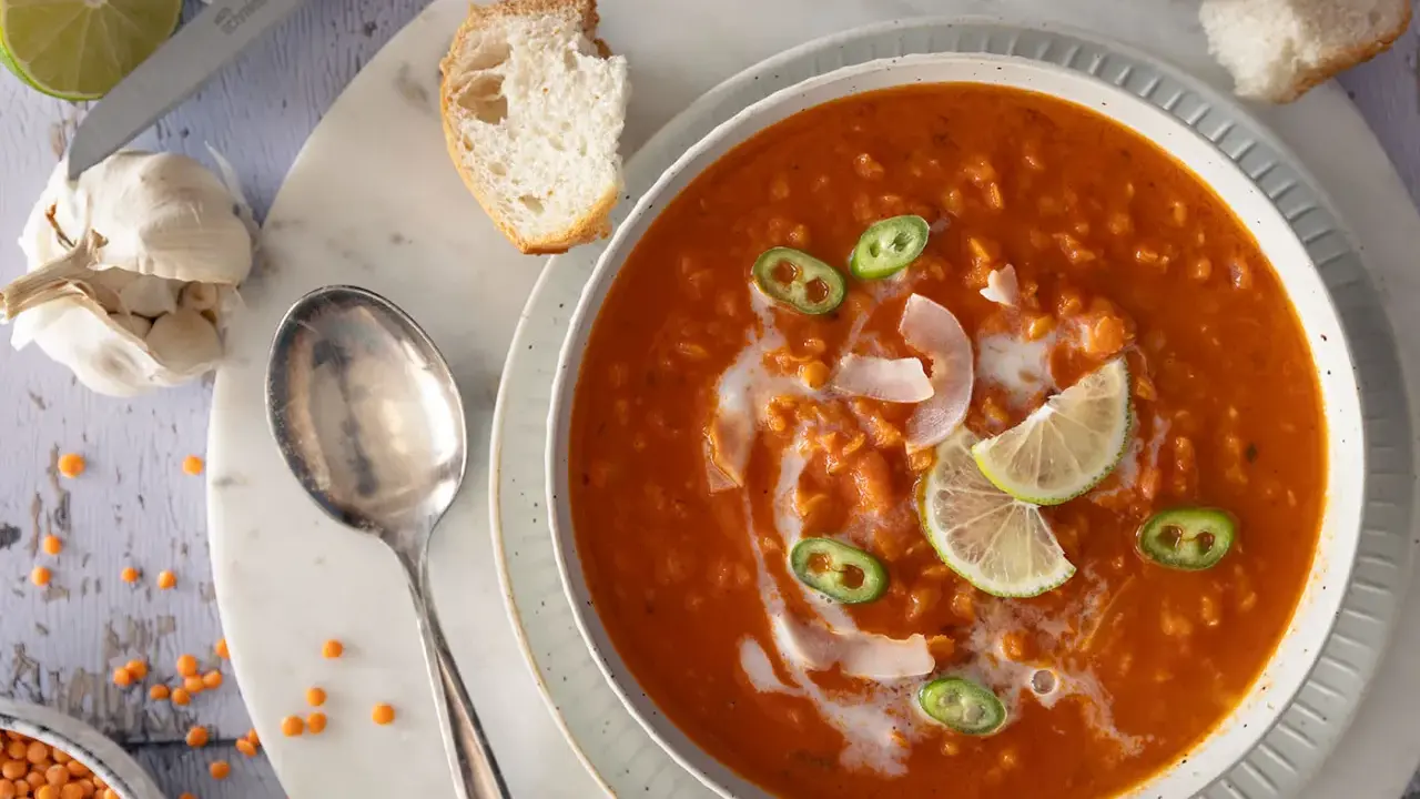 Eine cremige rote Linsensuppe mit Kokosmilch, garniert mit Limettenspalten und Jalapeños. Dazu gibt es knuspriges Brot.