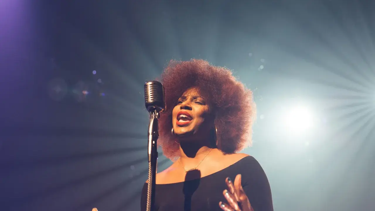 Kobieta z burzą afro włosów śpiewa do mikrofonu, jej głos jest niczym unchained melody, wolny i pełen emocji.
