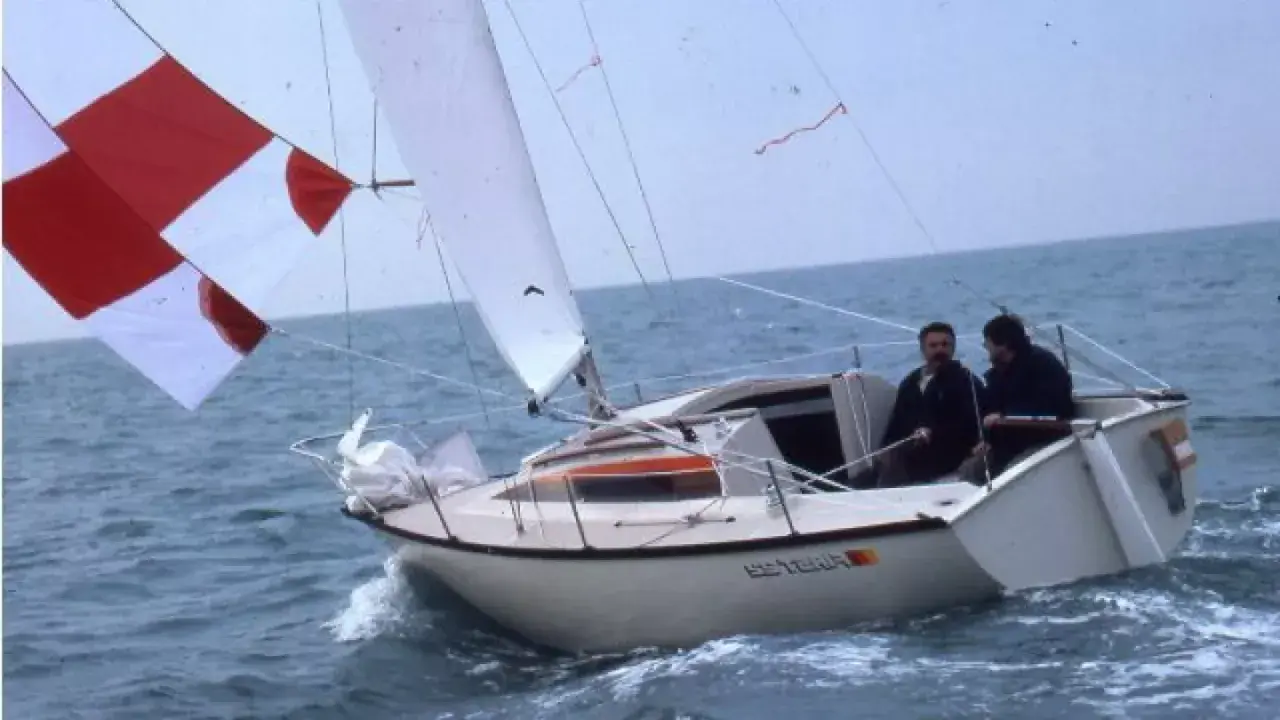 Deux hommes naviguent sur un voilier blanc, le "Esterel", avec des voiles rouges et blanches. Les premiers 22 avis sur ce bateau sont probablement très positifs.
