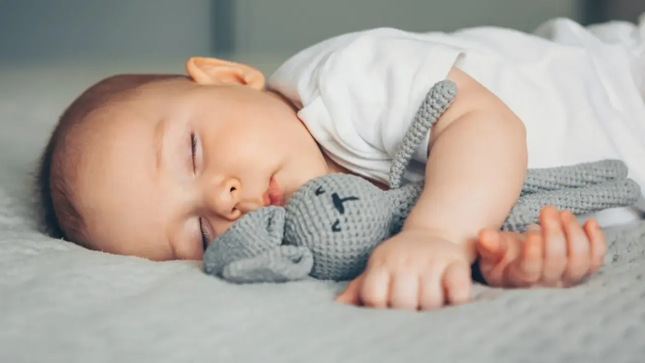 Ein Baby schläft friedlich mit seinem Häschen-Spielzeug. Vielleicht ist es die berüchtigte 4 monats schlafregression, die es so müde macht.