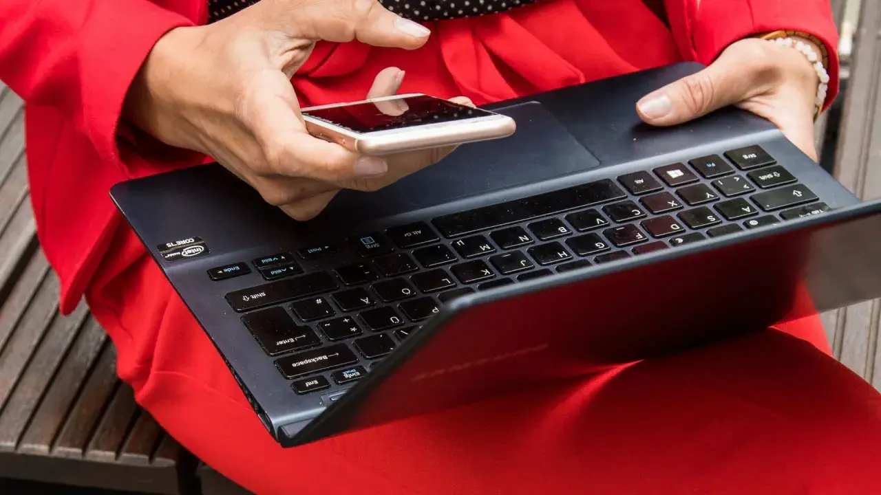 Besorgte Person prüft ihr Smartphone, nachdem ihr t-online Mail gehackt wurde. Sie hält es über eine Tastatur.