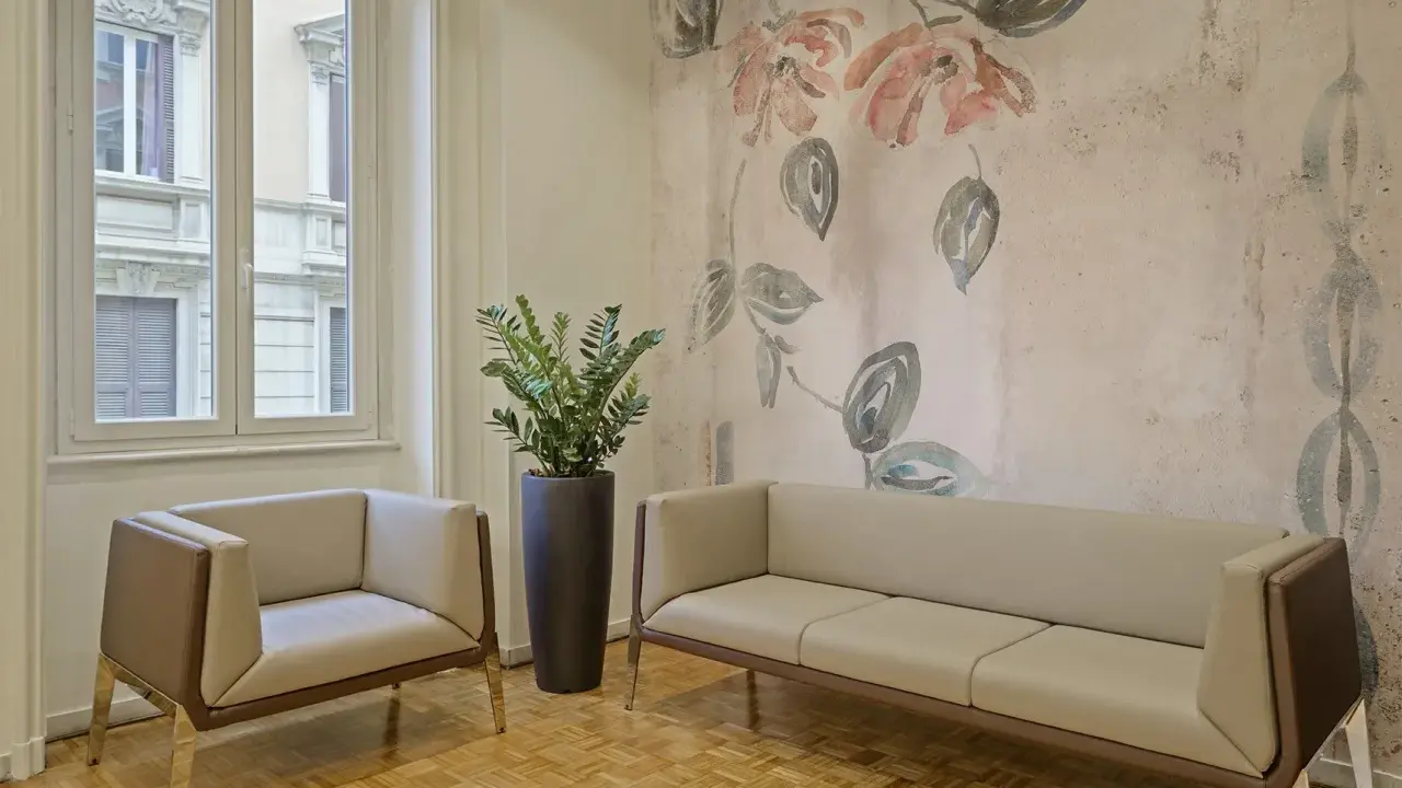 Eleganckie fotele i sofa na tle tapety z motywem kwiatowym. Czy można kleić tapetę na tapetę? Tutaj wygląda to stylowo.