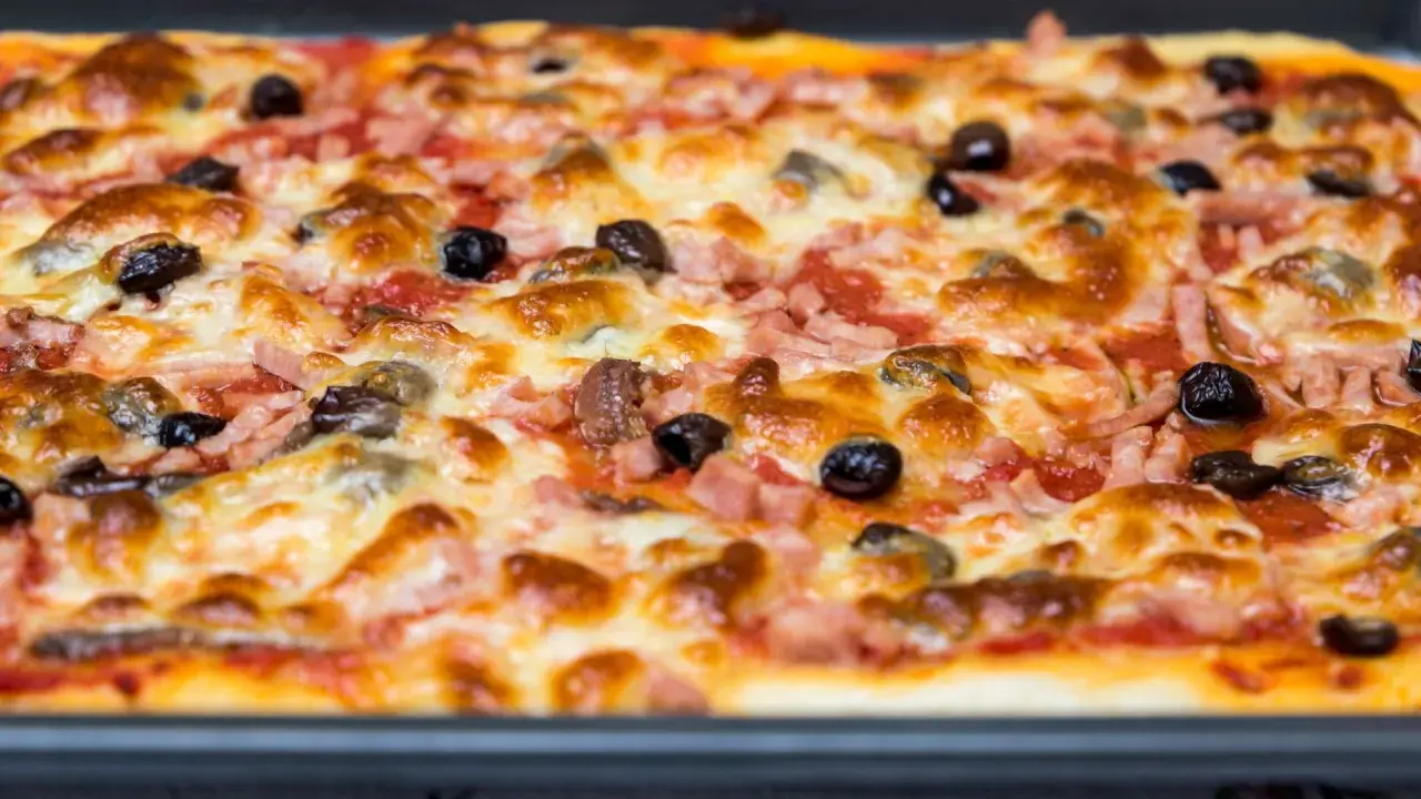 Une pizza rectangulaire garnie de jambon, d'olives et de fromage fondant. Parfait pour savoir que faire avec une pâte à pizza rectangulaire !