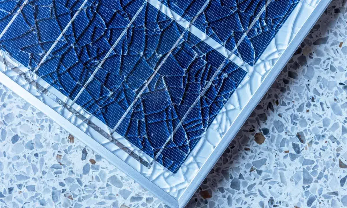 Gros plan sur un vitre panneau solaire brisé, ses fragments bleus reflétant la lumière sur un fond moucheté.