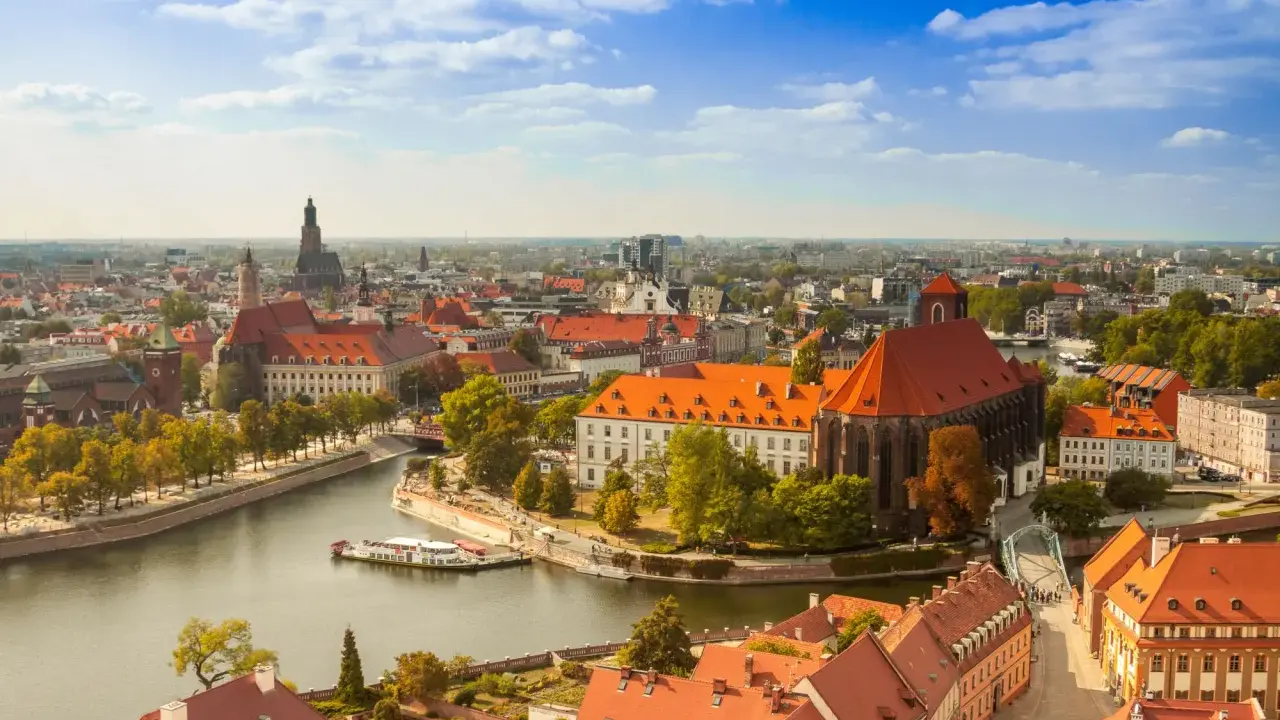 Widok na Ostrów Tumski we Wrocławiu, idealne miejsce na city break z Wrocławia. Rzeka, zabytkowe budynki i błękitne niebo.