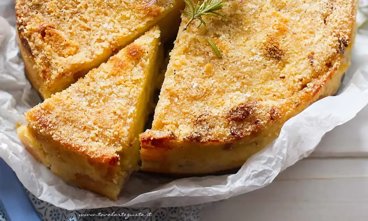 Delizioso gateau di patate dorato e croccante, guarnito con rosmarino fresco. Una fetta è già stata tagliata, invitando ad assaporare questo piatto saporito.