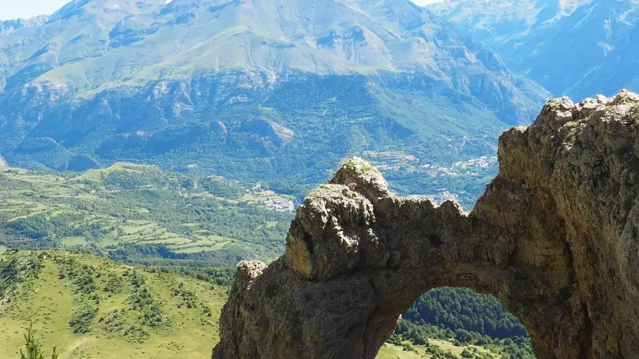 Arco natural en el valle de Tena, con vistas a montañas y un pueblo. Imagina a niños explorando este paisaje.