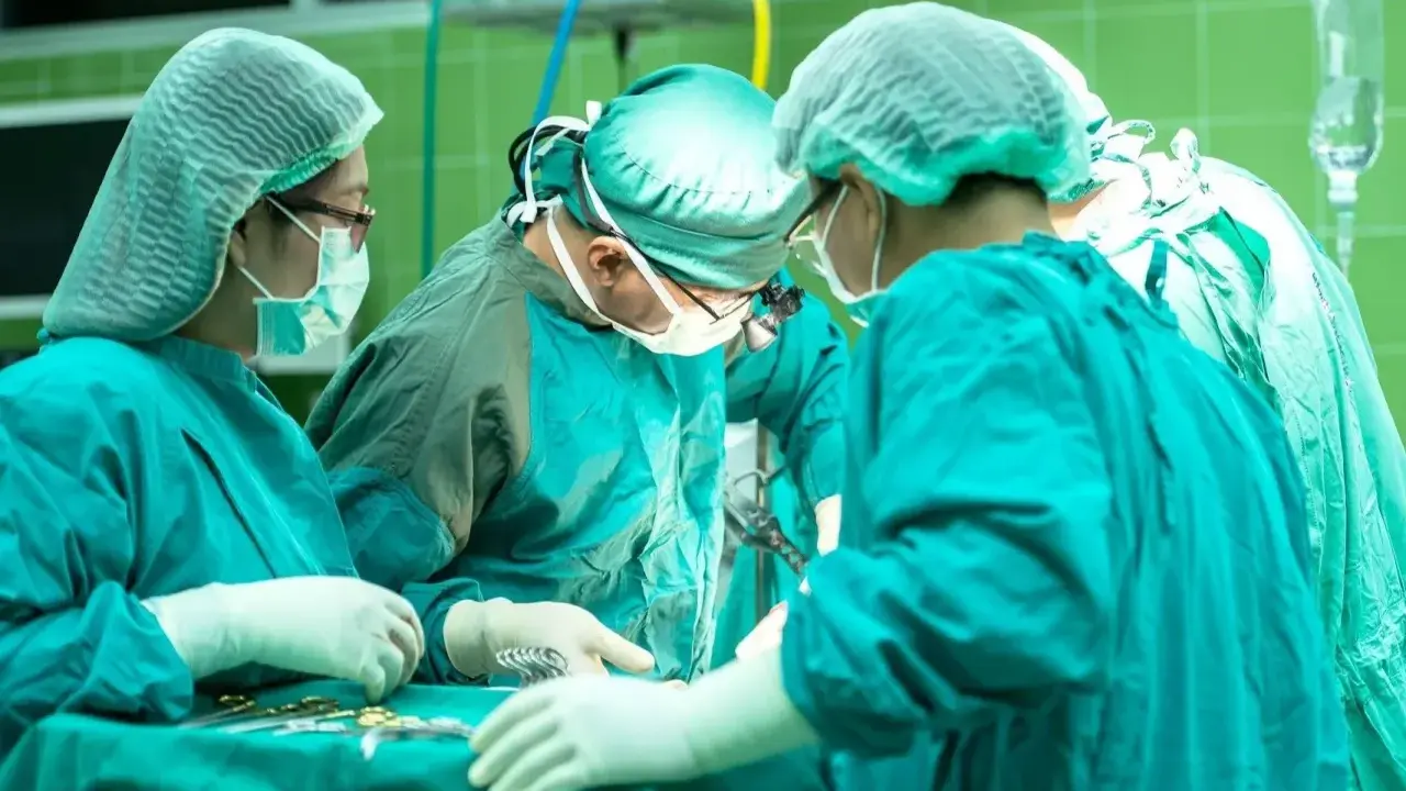 Zespół chirurgów w zielonych fartuchach i czepkach przeprowadza skomplikowaną operację głosu.