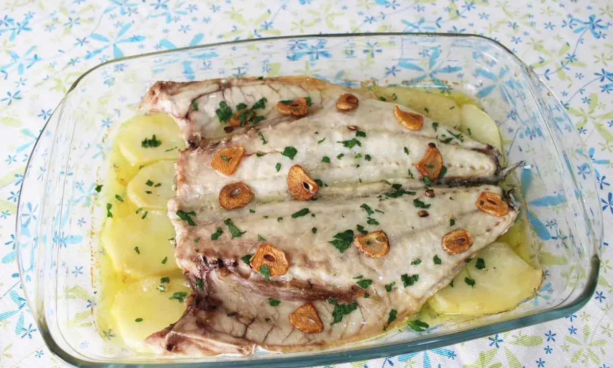 Lubina a la espalda horneada con patatas, ajo y perejil en una fuente de cristal.