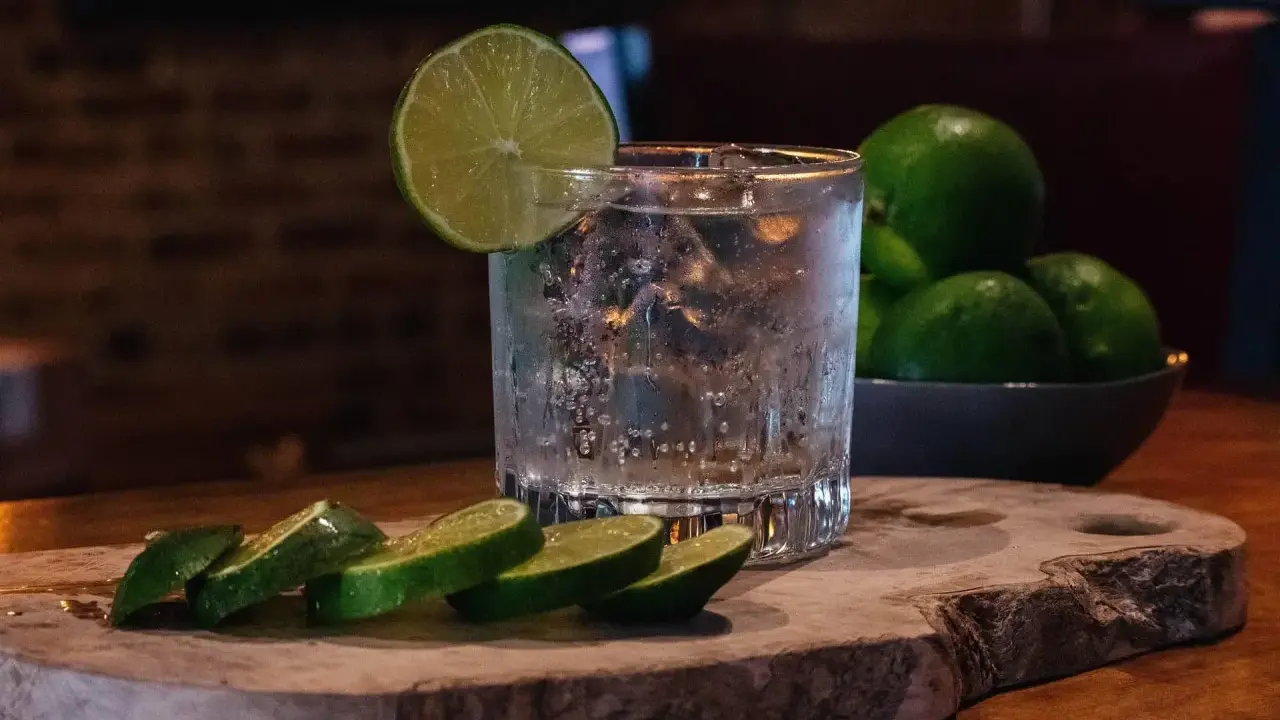 Erfrischendes Glas mit Eis, Limettenscheiben und einer Schale voller Limetten – perfekt für ein Tonic Water Rezept.