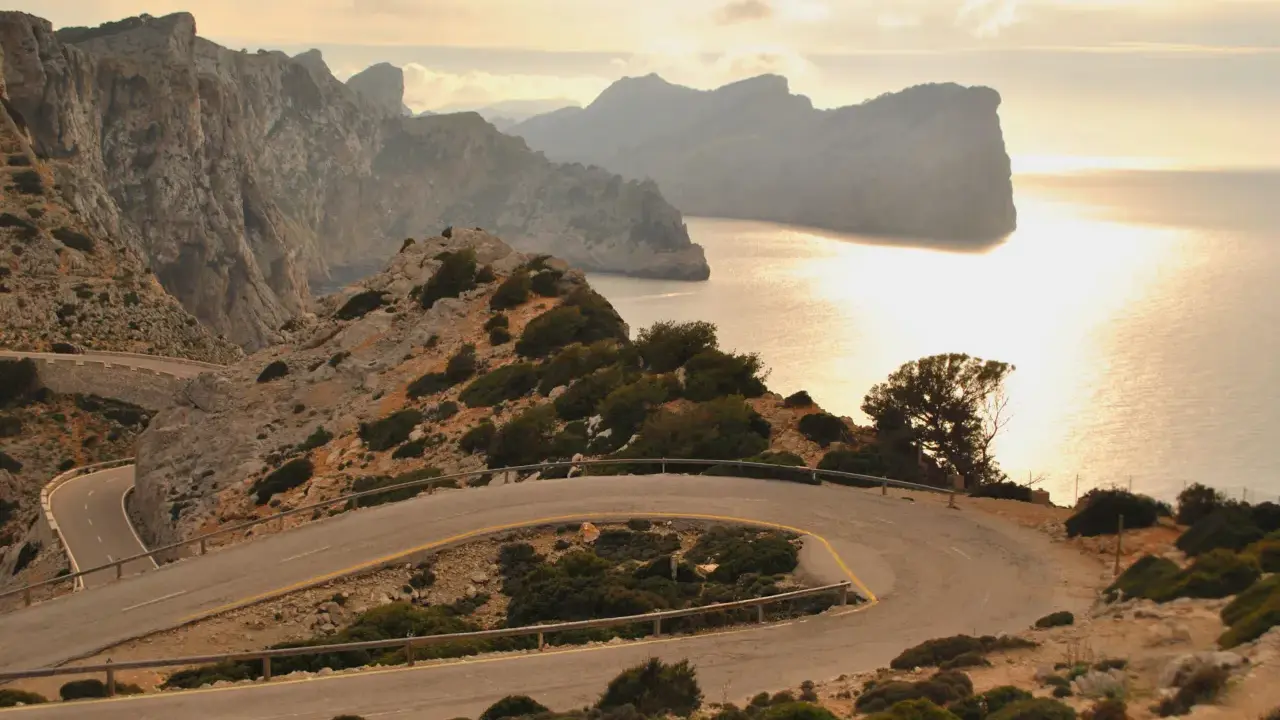 Kręta droga prowadzi do Playa de Formentor, otoczona skalistymi zboczami i morzem o zachodzie słońca.