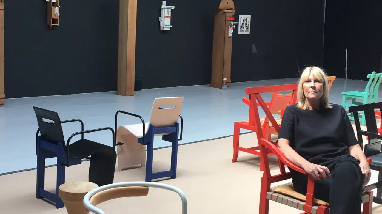 En kvinna sitter i en röd stol i en utställning med möbler av John Kandell.