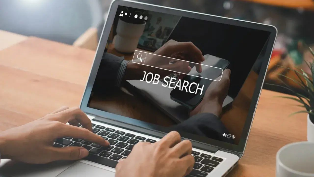 Ręce wpisują "JOB SEARCH" na laptopie. Praca wre, szukamy nowych możliwości.