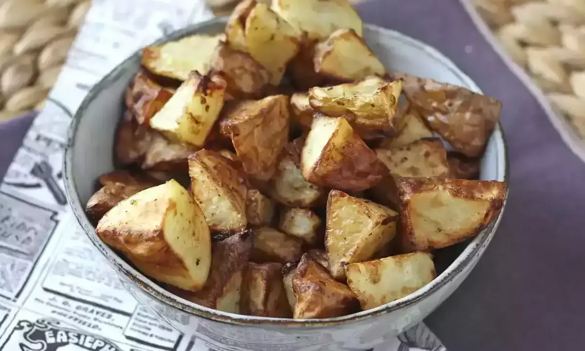 Patate dorate e croccanti in friggitrice ad aria, servite in una ciotola su carta di giornale.