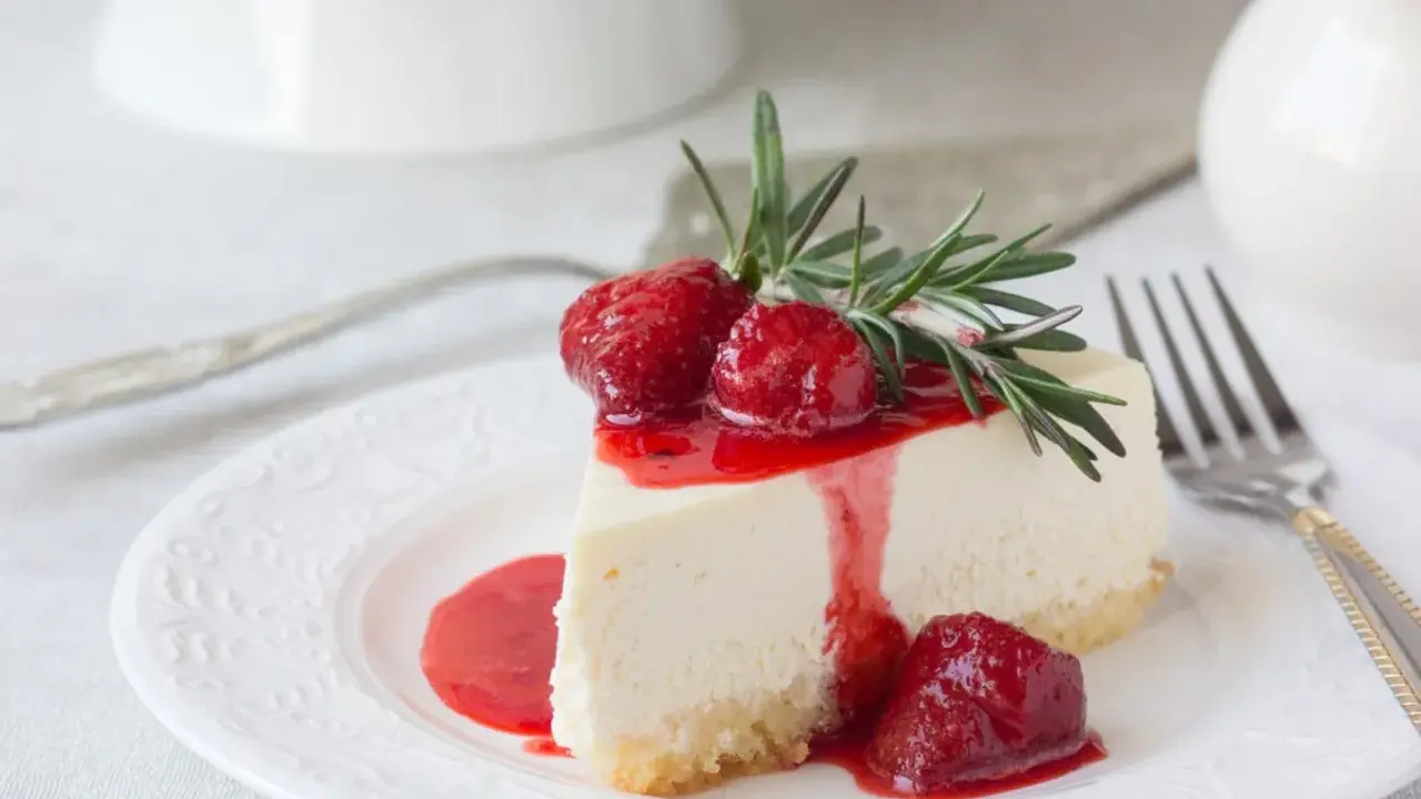 Ein Stück cremige Philadelphia Torte mit Erdbeersauce und frischen Erdbeeren, garniert mit Rosmarin.