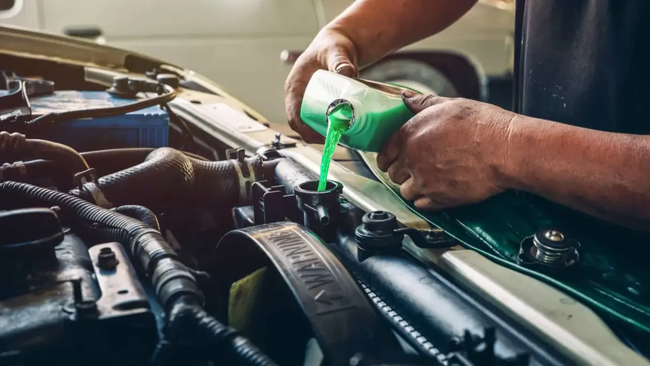 Mecánico rellenando refrigerante verde en el radiador de un coche, solucionando una posible fuga de gas aire acondicionado.