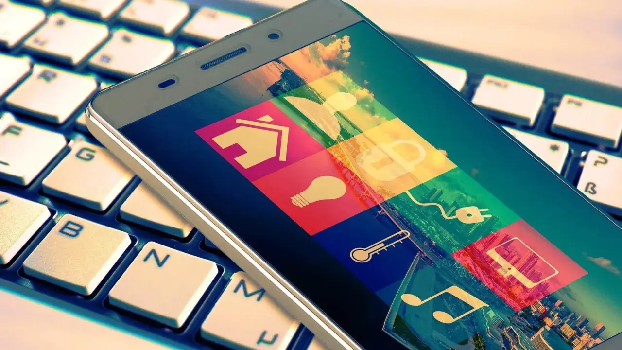Smartphone mit Smart-Home-Symbolen auf Tastatur. Das Hacken Bedeutung wird hier durch die vielen Icons symbolisiert, die Zugang zu verschiedenen Bereichen des Lebens gewähren.