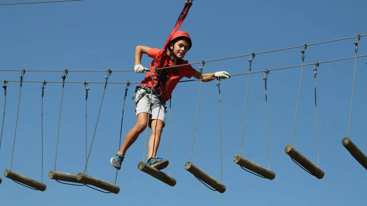 Niño con casco naranja cruza tirolinas en San Pablo de los Montes, disfrutando de la aventura.