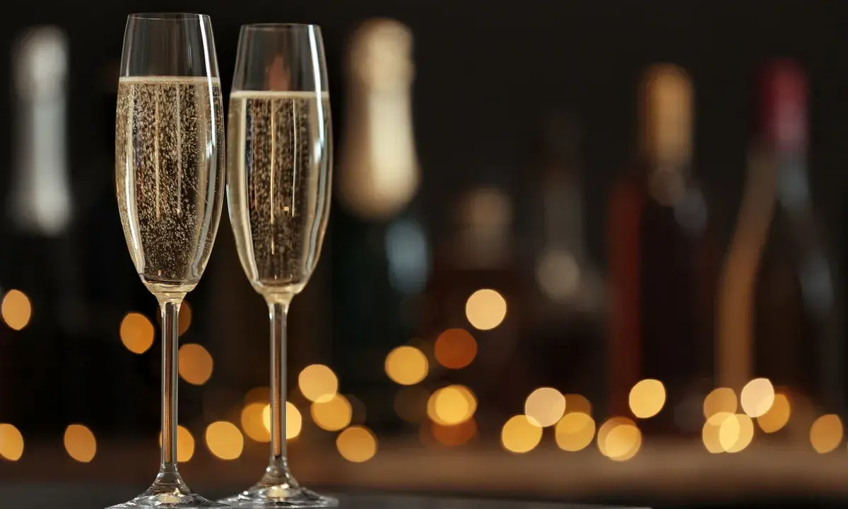 Zwei Sektgläser mit sprudelndem Sekt, im Hintergrund unscharfe Flaschen und Lichter. Ein krug 169 für besondere Anlässe.