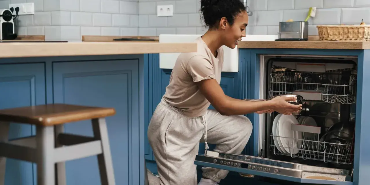 Une femme charge son lave-vaisselle encastrable. Elle place une casserole dans le panier inférieur.