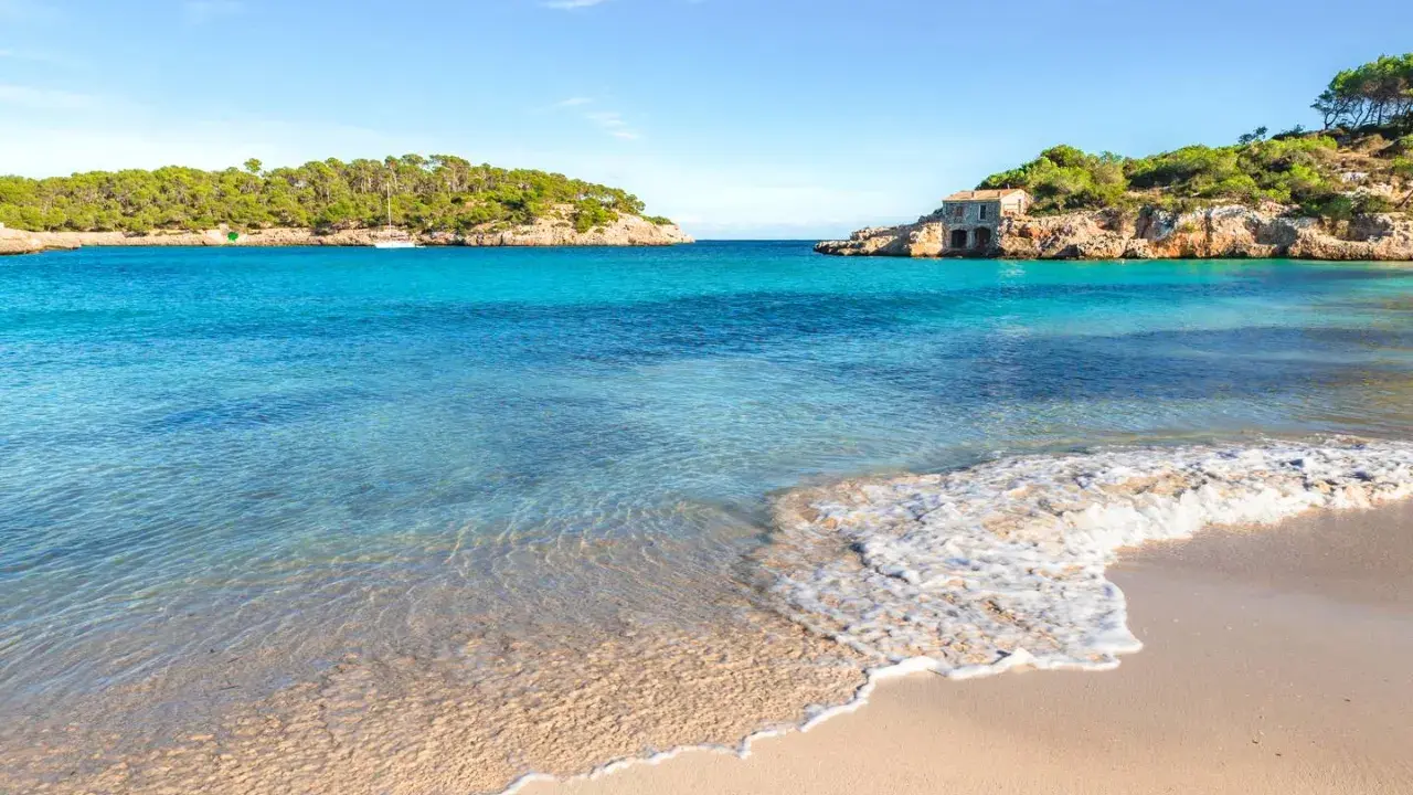 Türkisfarbenes Meer, Sandstrand und felsige Küste mit einem kleinen Haus auf Mallorca.