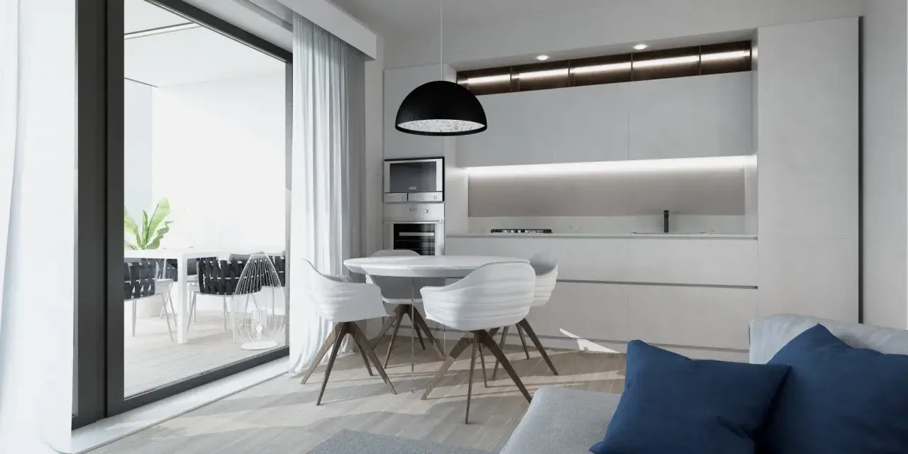 Interni luminosi di una casa di design con cucina moderna, tavolo rotondo e sedie bianche. Si intravede un terrazzo con piante.