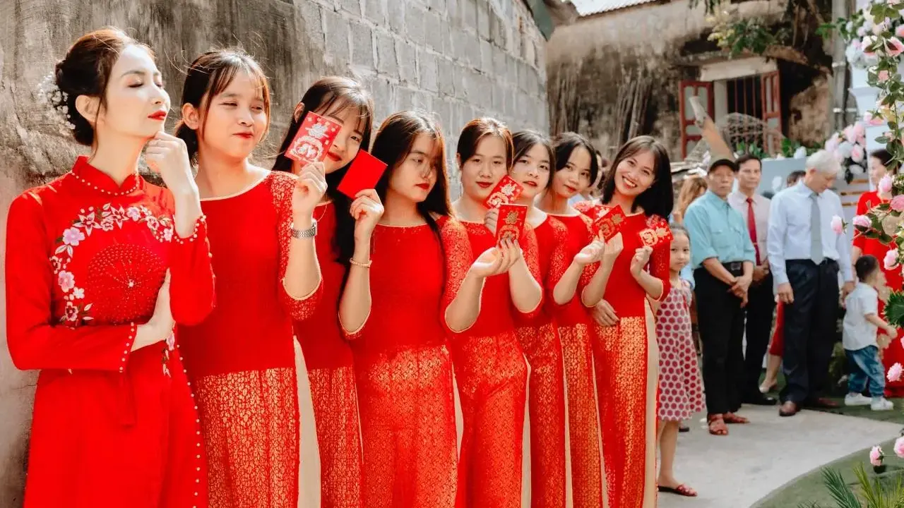 Novias y damas de honor con trajes rojos tradicionales, sosteniendo sobres rojos, celebrando una boda china.
