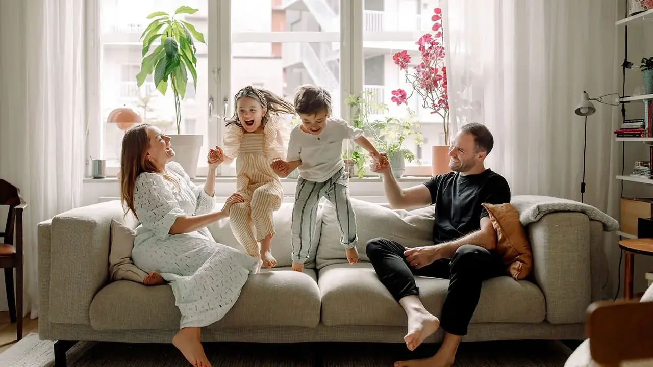 Familjen hoppar glatt på soffan i detta hemma hos reportage. Barnen skrattar högt medan föräldrarna ler.