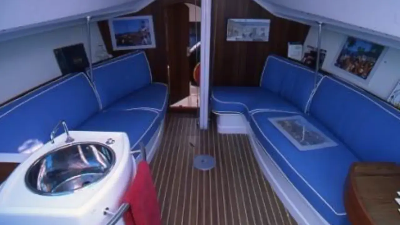 Intérieur du JOD 35, avec banquettes bleues, évier en inox et parquet en bois. Prêt pour une nouvelle aventure en mer.