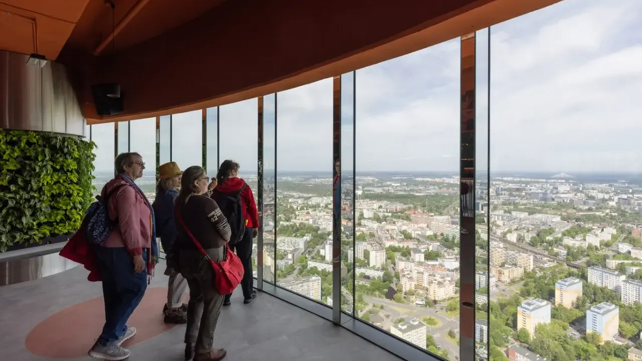 Grupa turystów podziwia panoramę miasta z tarasu widokowego najwyższego budynku we Wrocławiu.