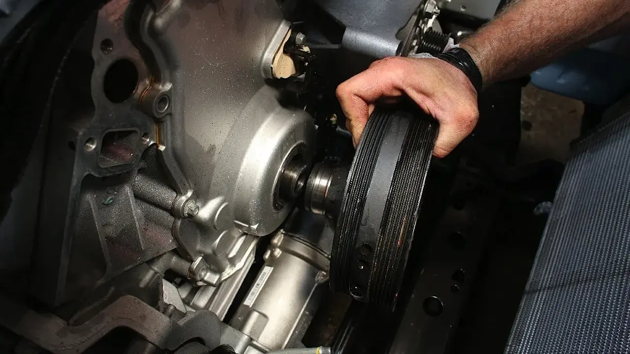 Mano retirando la polea del cigüeñal rota de un motor.