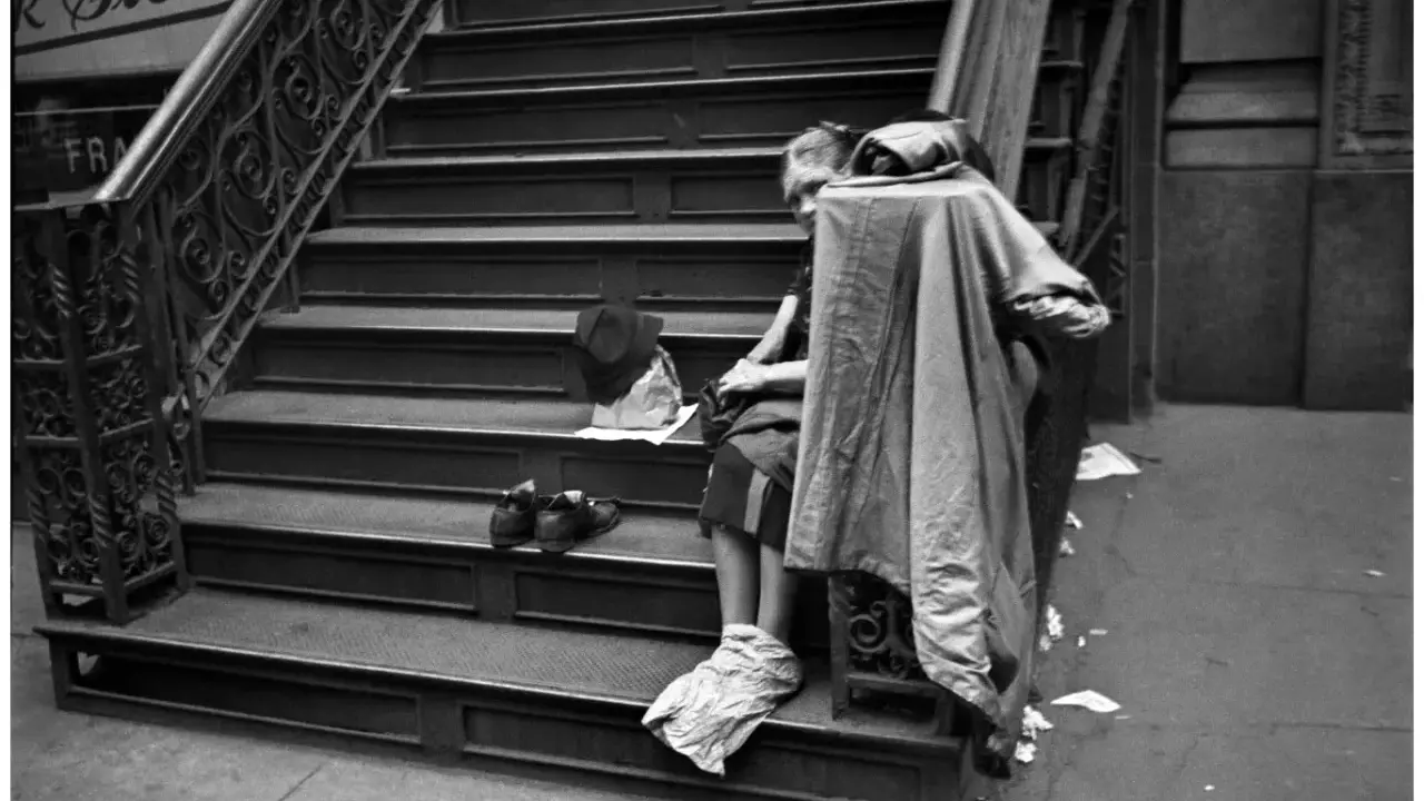 Una persona seduta sulle scale, con scarpe e cappello accanto. Un'immagine che evoca le cartier bresson foto famose, catturando un momento di vita urbana.