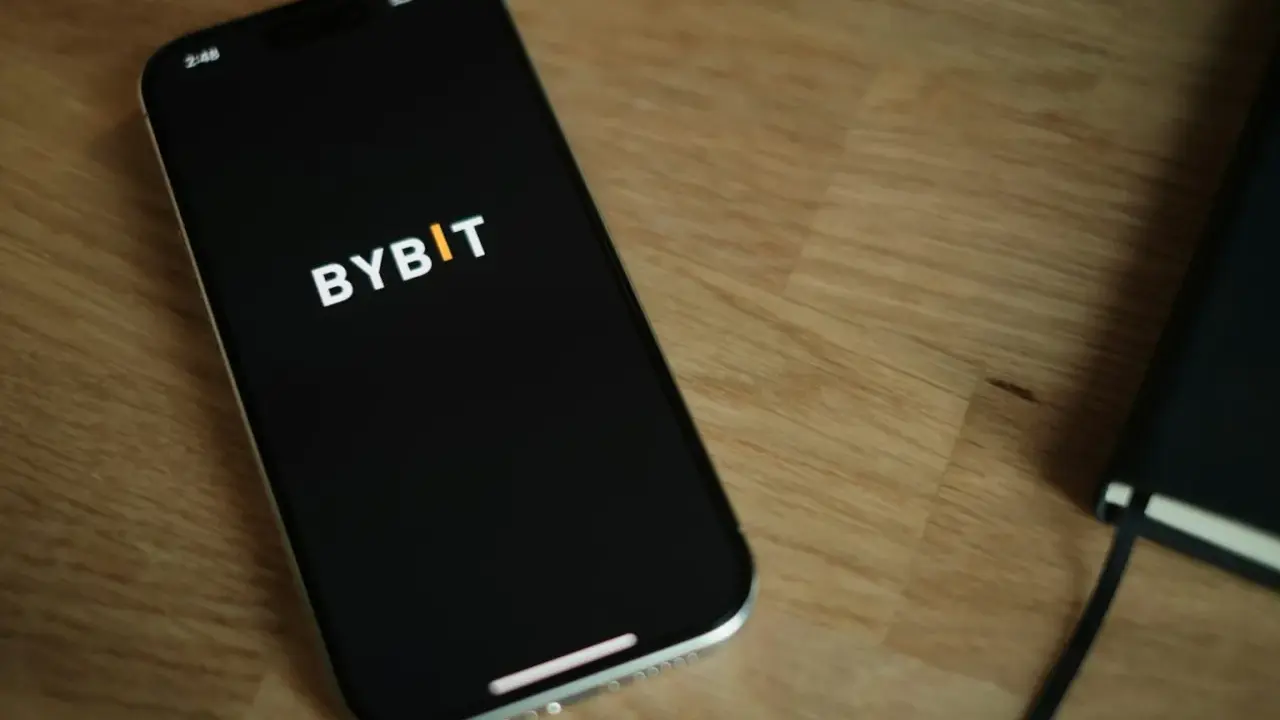 Smartfon z logo Bybit na ekranie, obok notatnik. Analiza bybit prowizje na urządzeniu mobilnym.