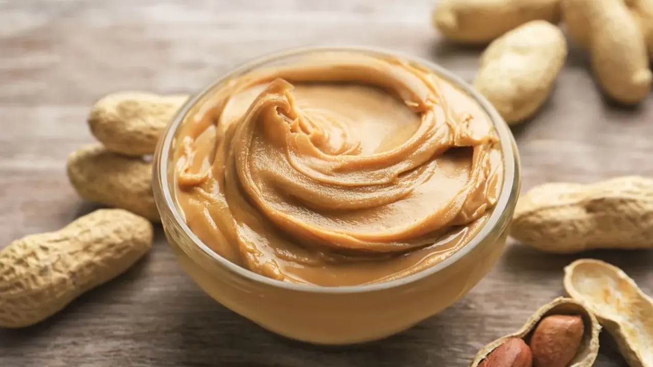 Cremige Erdnussbutter in einer Schüssel, umgeben von Erdnüssen. Ein Beweis dafür, dass erdnussbutter gesund sein kann, wenn sie in Maßen genossen wird.