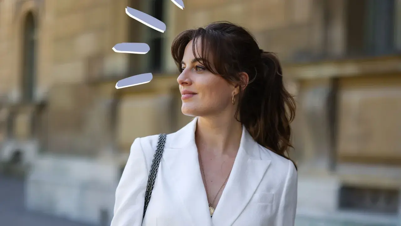 Frauen mit Curtain Bangs stylen ihre Haare lässig zu einem Pferdeschwanz. Der weiße Blazer unterstreicht den eleganten Look.