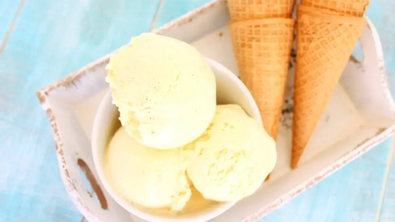 Tres bolas de cremoso helado de vainilla en un cuenco blanco, junto a conos de galleta sobre una bandeja.