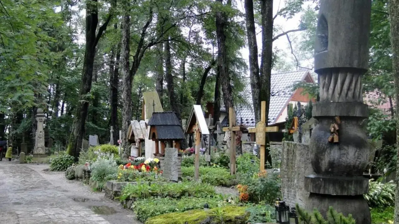 Cmentarz w Zakopanem, pełen drewnianych krzyży i rzeźb, otoczony zielenią.