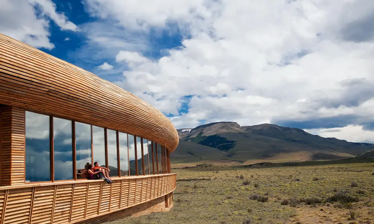 Coppia seduta su una terrazza di **edifici in legno famosi**, con vista su un paesaggio montano e cielo nuvoloso.