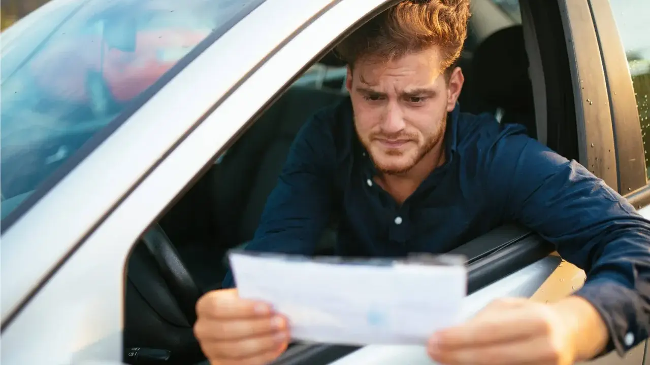 Hombre preocupado mira un papel, preguntándose cuanto tarda una multa en aparecer en mi DGT.